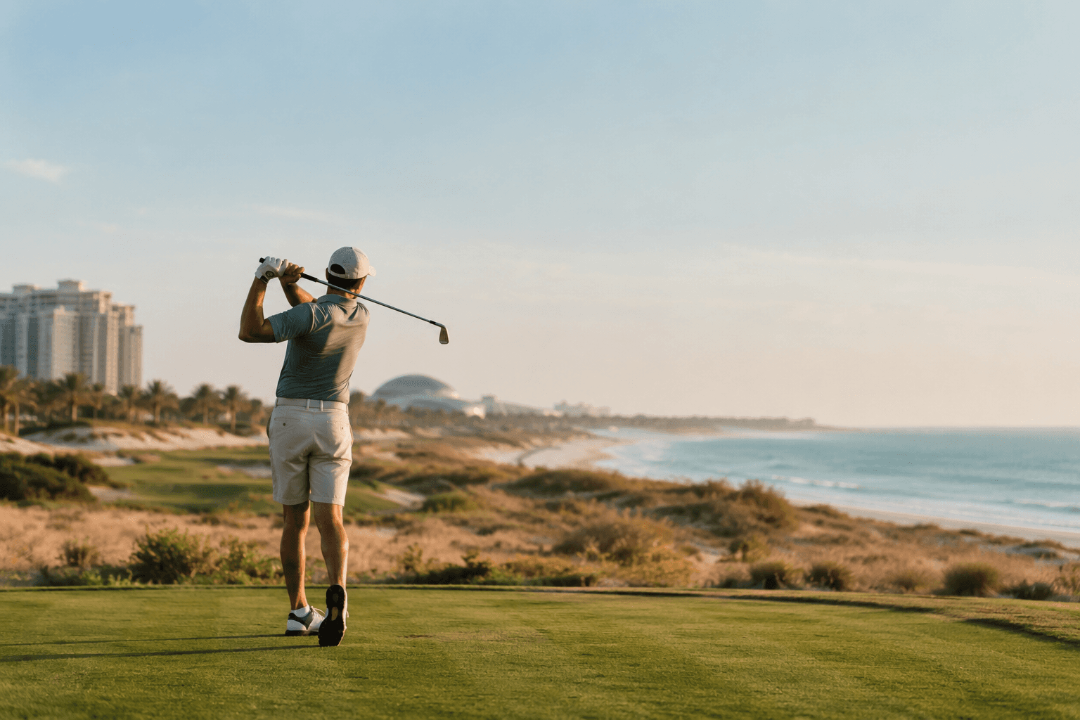 A golfer holding the finish of a swing on a coastal course near Saadiyat Island