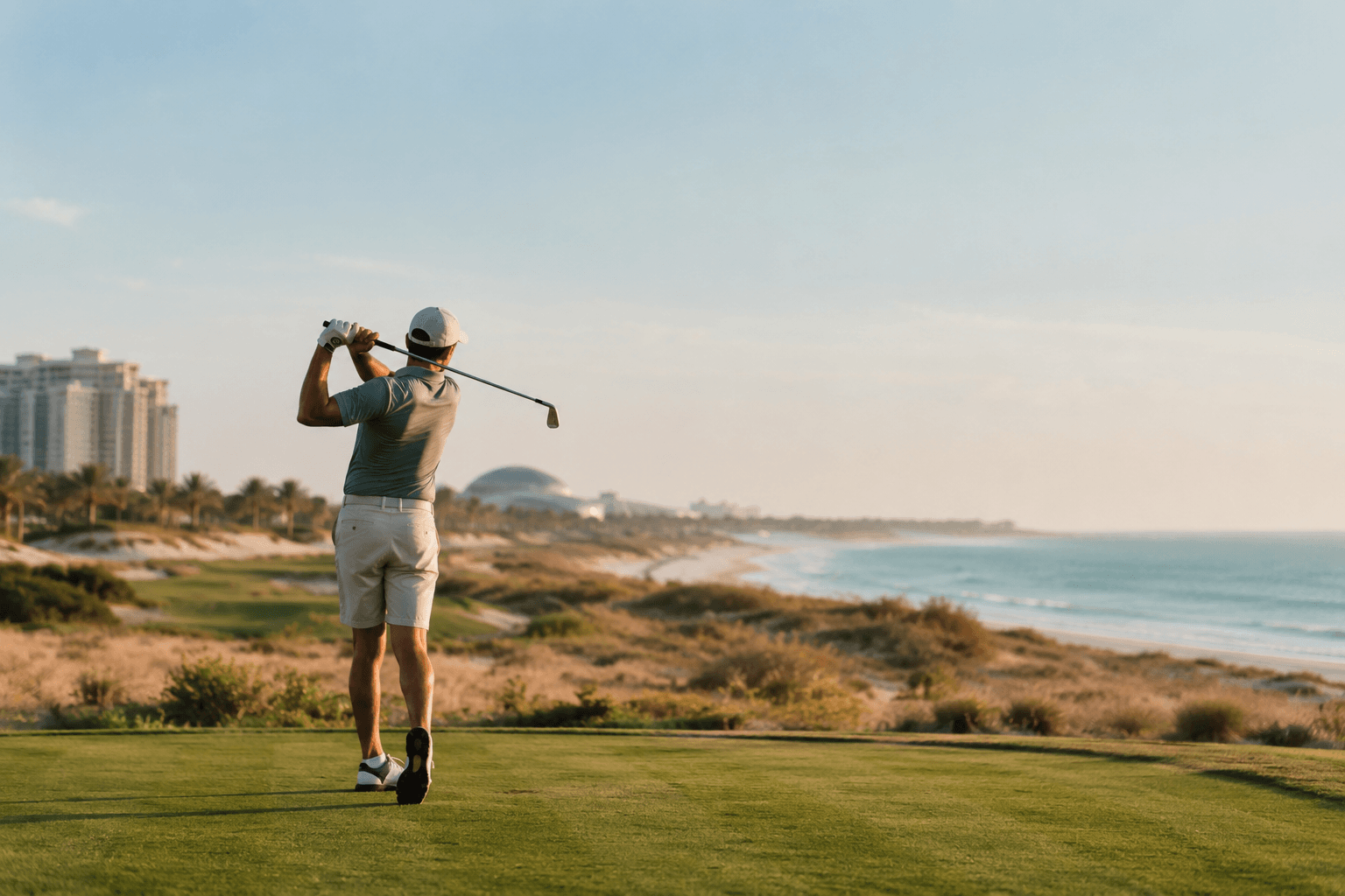 A golfer holding the finish of a swing on a coastal course near Saadiyat Island