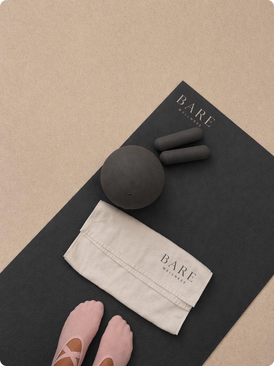 A Bare Wellness mat laid out with a toning ball, hand weights, towel and grip socks